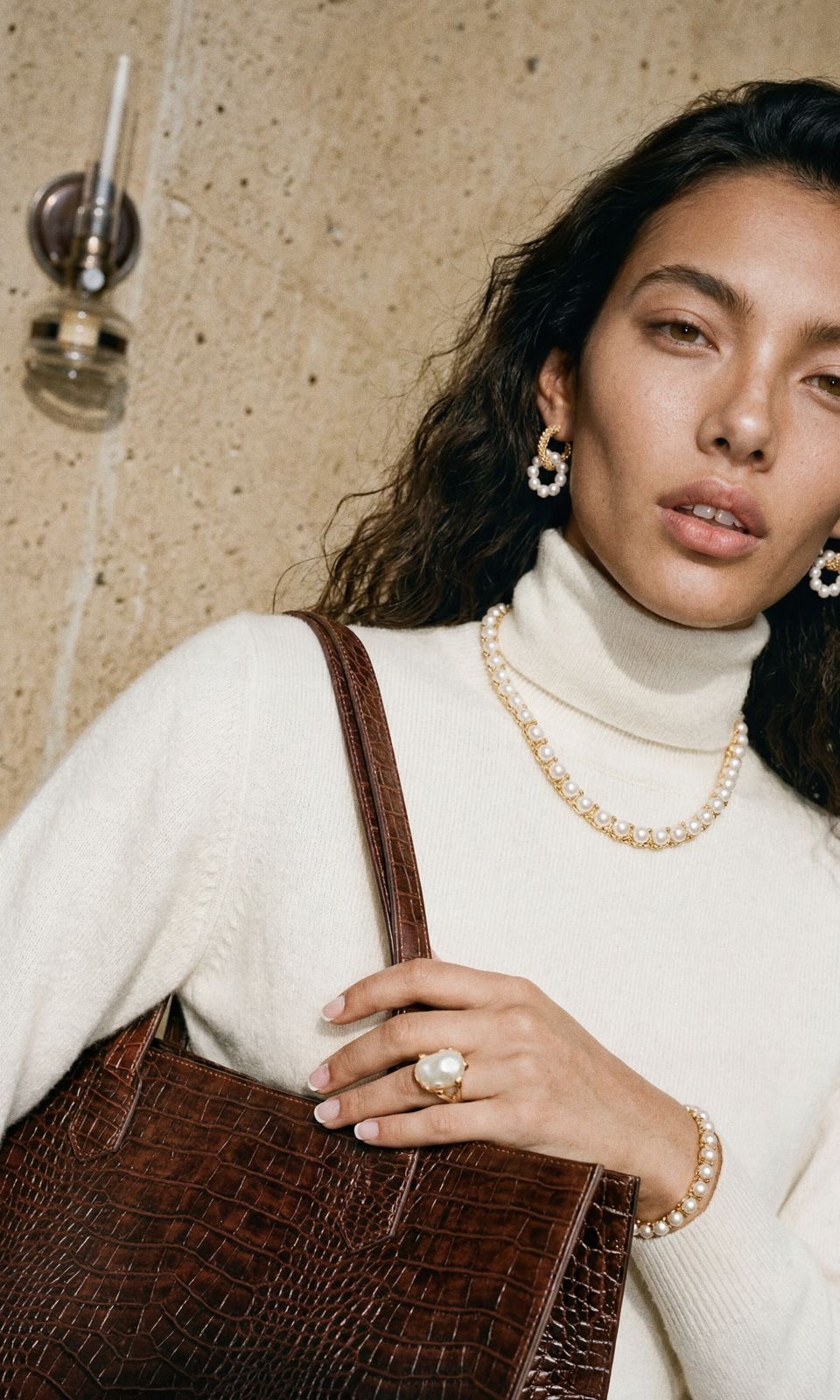 Three-quarter editorial shot — model carrying a brown croc-embossed tote, wearing a layered pearl necklace, pearl bracelet and baroque pearl ring.