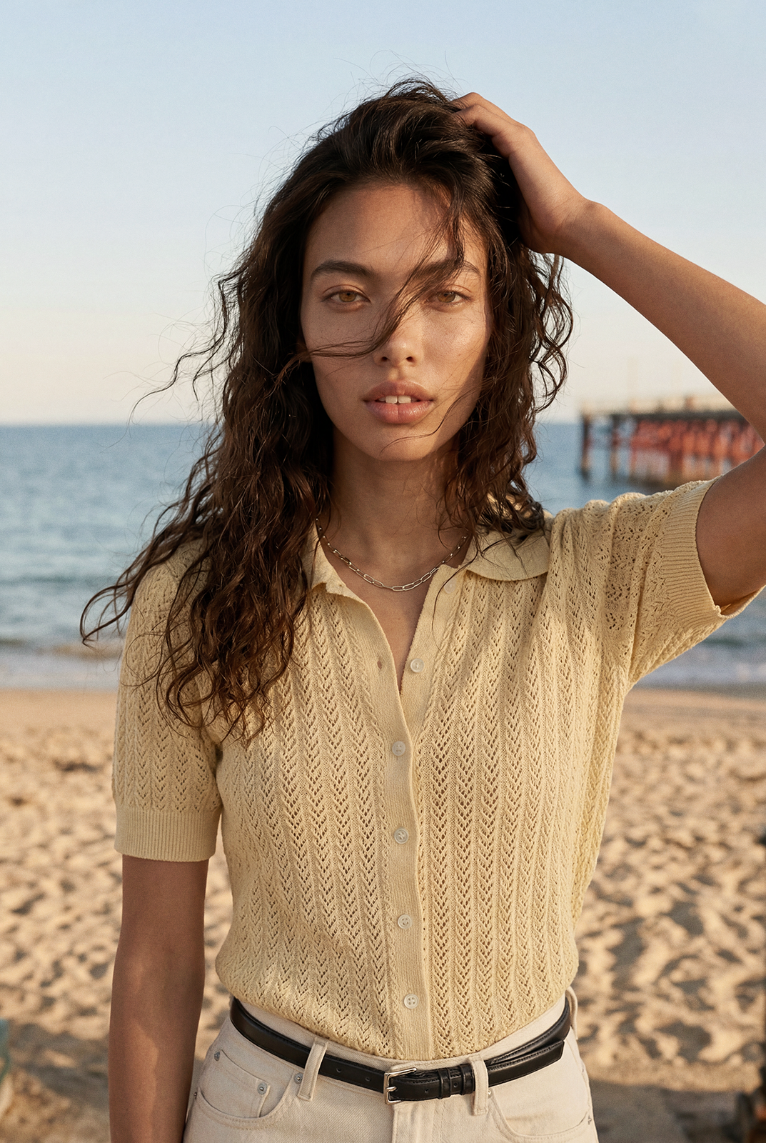 Close portrait of a woman at the beach in a cream knit polo shirt, hair blown by the wind, head centered.