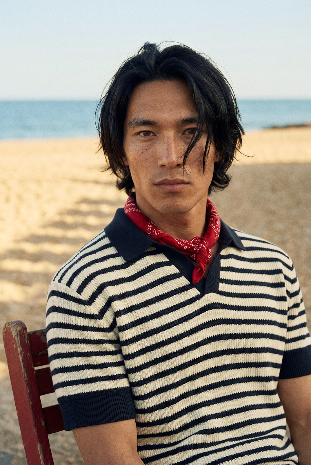Close portrait of a man at the beach in a striped knit polo with a red scarf.