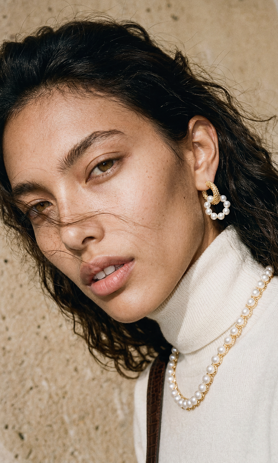 Wind-blown portrait of a model in cream cashmere wearing a pearl choker, gold-and-pearl hoops and a baroque pearl ring.